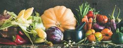 Fresh produce on counter with dark background with central squash, corn, cabbage, heirloom tomatoes
