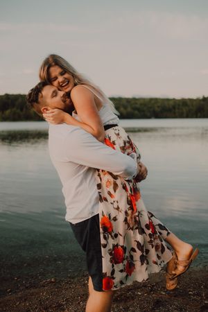 Loving man carrying happy woman on hands on shore