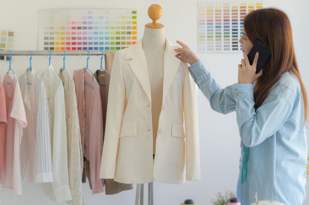 Young tailor working on a phone with a model mannequin in a workshop.