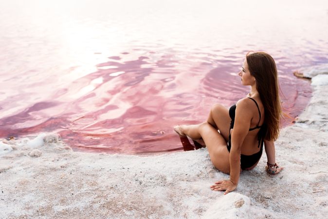 Tranquil woman in swimwear sunbathing on shore of pink lake