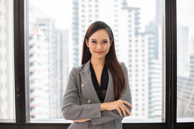 Confident Asian business woman standing by office window