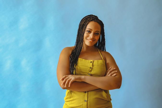 Smiling female with long braided hair and arms crossed in yellow one piece