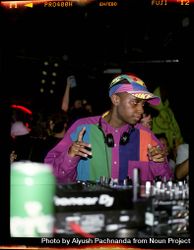 Young male DJ in colorful retro 90s garb performs on mixer and turntables 0v3xB5