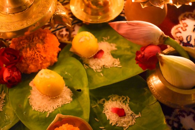 Close-up shot of yellow ladoo on a bed of rice on tree leaf surrounded by flowers