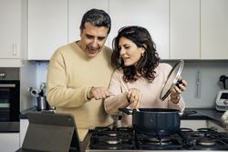 Authentic couple cooking together using online recipe on tablet in modern kitchen