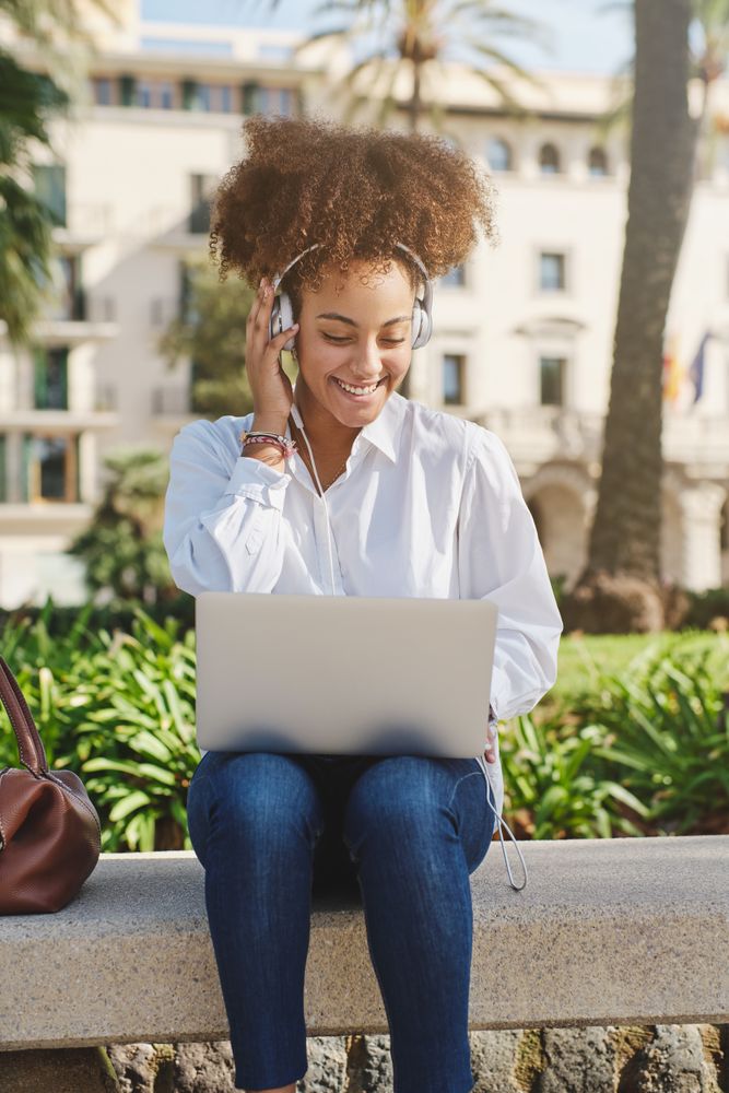 Smiling Black woman with netbook and headphones on street
