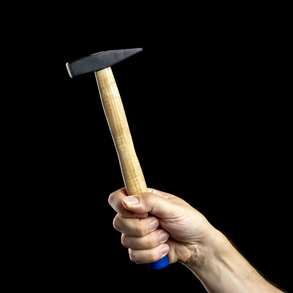 Hand holding a hammer on a dark background.