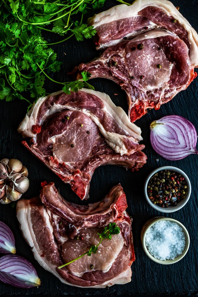 Top view of raw pork steaks with herbs, garlic, onion, salt and pepper 