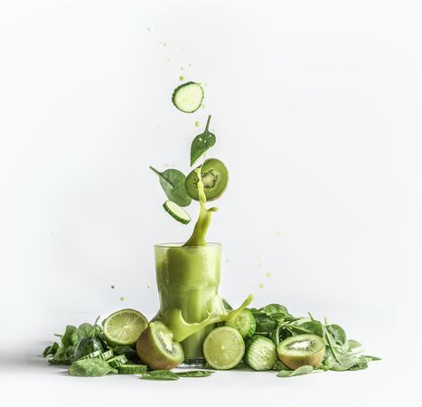 Splashing of green smoothie in glass with and flying ingredients: cucumber,kiwi and spinach leaves