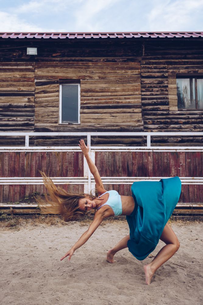 Flexible woman in colorful skirt dancing at rural paddock
