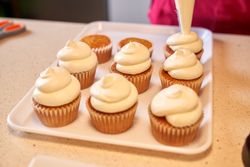 Crop person decorating cupcakes with whipped cream