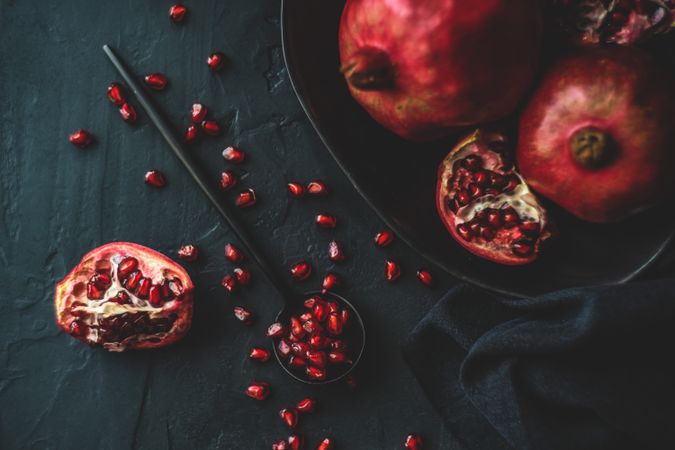 Spoon with pomegranate seeds next to fruit bowl on dark surface