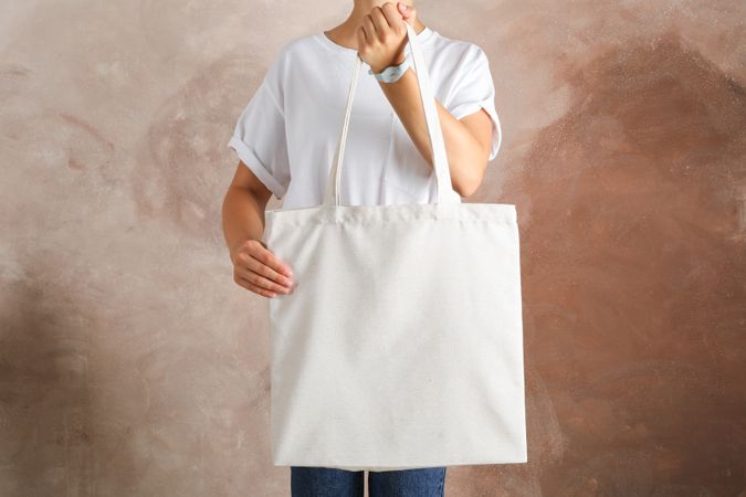 Young woman holding tote bag against brown background, empty space
