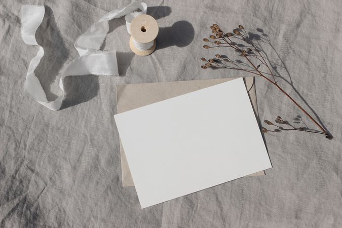 Blank Christmas greeting card, invitation mockup with dry flower and craft paper envelope in sunlight