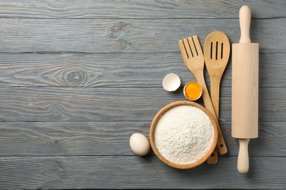 Kitchen cutlery, flour and eggs on gray wooden background