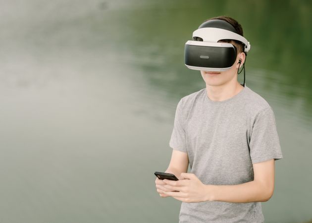 Young teenager with virtual reality glasses and smart phone outdoors