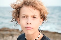 Boy wearing shell necklace looking at camera at beach