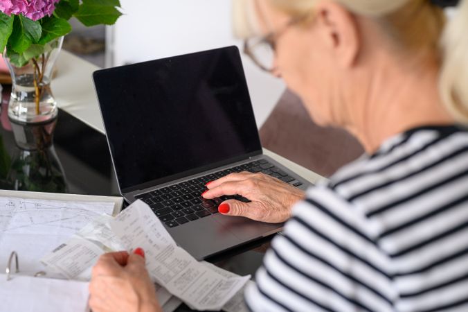 Mature woman watching bills and mail bank notice, sitting at living room table at home