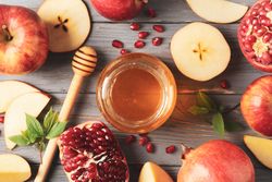 Top view of honey pot surrounded by slices apples and pomegranate on grey table