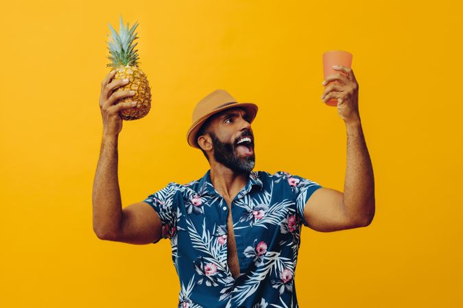 Happy male holding up a pineapple and orange cup