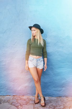 Full length shot of stylish young woman standing against blue wall and looking away