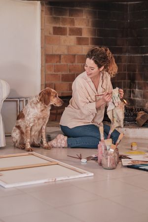 Young woman wiping paintbrush and looking at dog