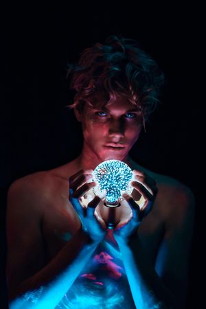 Topless young man holding crystal ball lamp against dark background