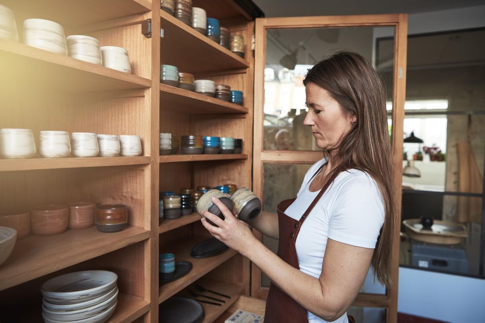 Woman in leather apron holding handmade cups in her shop