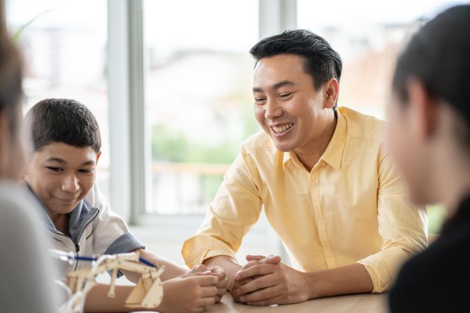 Male teacher in yellow shirt smiling with students around table