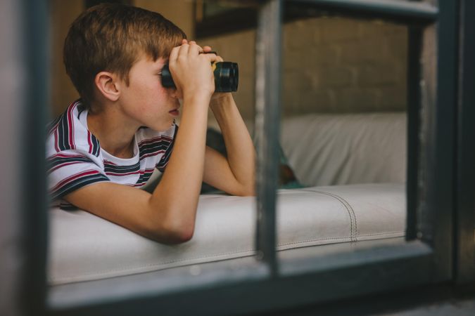 Curious boy looking out the window with binocular