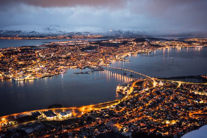 Majestic view of night city against snowy mountains in overcast weather