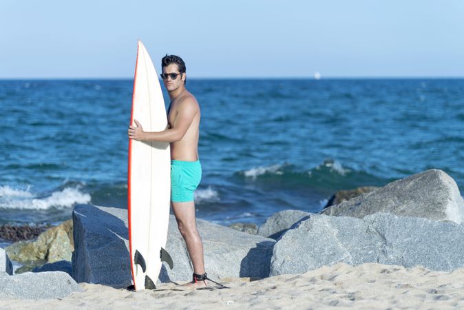 Male surfer standing on rock near ocean with board