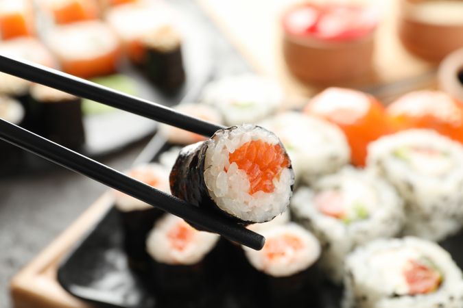 Chopsticks with delicious sushi roll, close up. Japanese food
