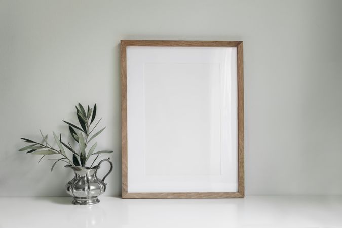Blank vertical wooden picture frame mockup of olive tree branches in elegant silver jug vase