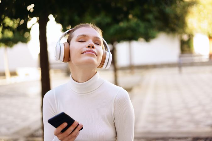 A Young Woman Happily Enjoying Music Outdoors while Wearing Headphones and Using Her Smartphone