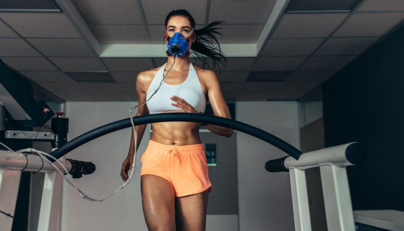Female athlete with mask running on treadmill to analyze her fitness performance