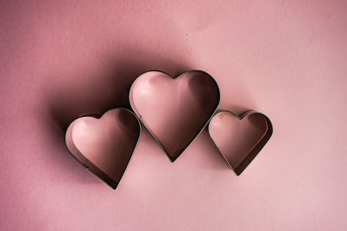 Three heart shaped cookie cutters on pink table