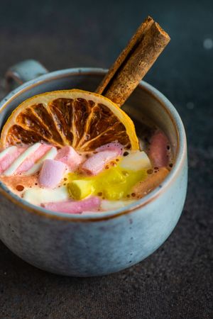 Close up of marshmallow drink in mugs with dried orange slice and cinnamon
