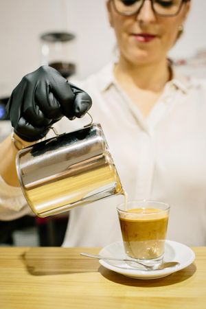 Barista pouring milk over coffee