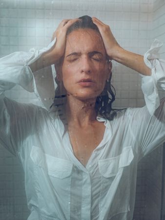 woman in wet shirt touching head under pouring water