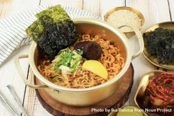 Brass pot full of noodles with seaweed, radish, onion and mushroom garnish 48my7b