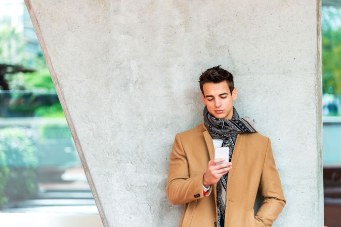 Young man in the center wearing winter coat looking at phone screen against cement pillar