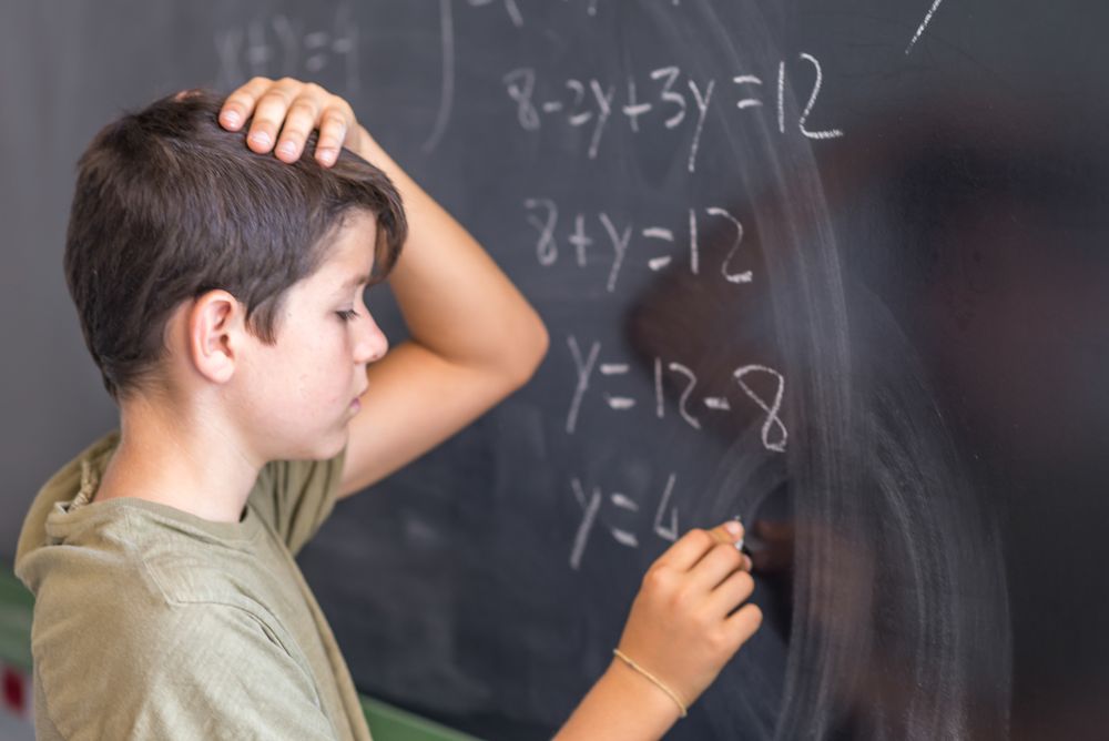Teenage male solving equation at chalk board