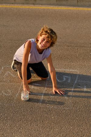 Cheerful boy drawing on asphalt ground