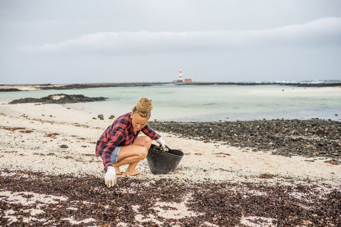Content modern woman picking litter from sandy seashore