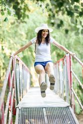 Smiling brunette female swinging herself on wooden bridge in forest