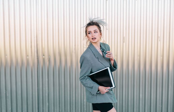 Woman with tablet in stylish suit standing nearby wall holding sunglasses