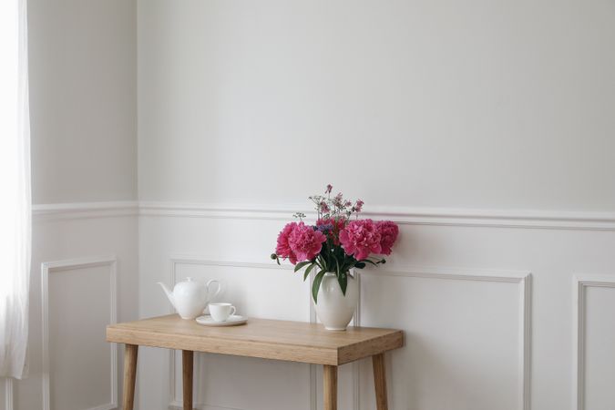 Calm home scene with vase with pink peonies flowers on wooden table with tea pot