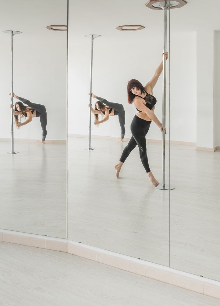 Flexible women dancing near pole in studio