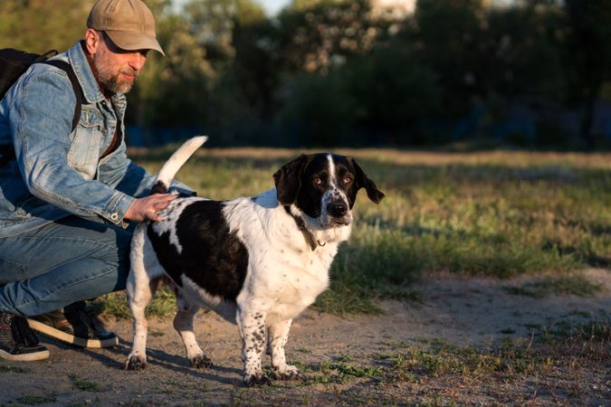 Man comforting hound dog in sunlit outdoor setting.